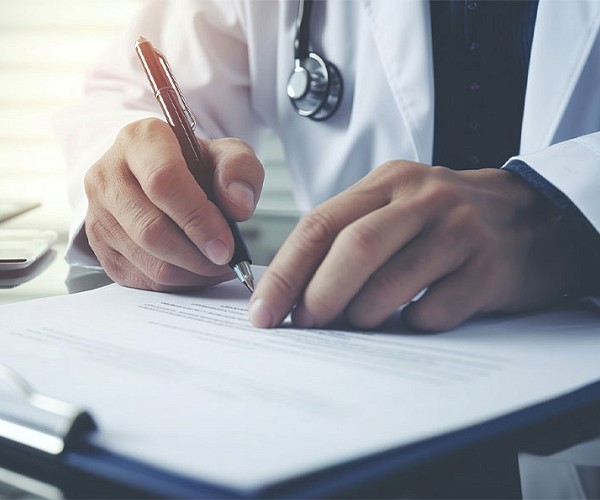 close up of some one writing on a clipboard wearing a lab coat